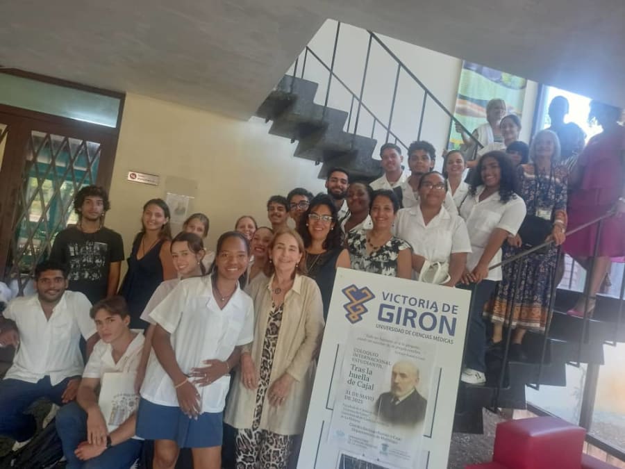 Grupo de estudiantes y profesionales de la salud posando en la Casa Estudiantil de la Universidad de Ciencias Médicas de La Habana, junto a un cartel que anuncia el Coloquio Internacional