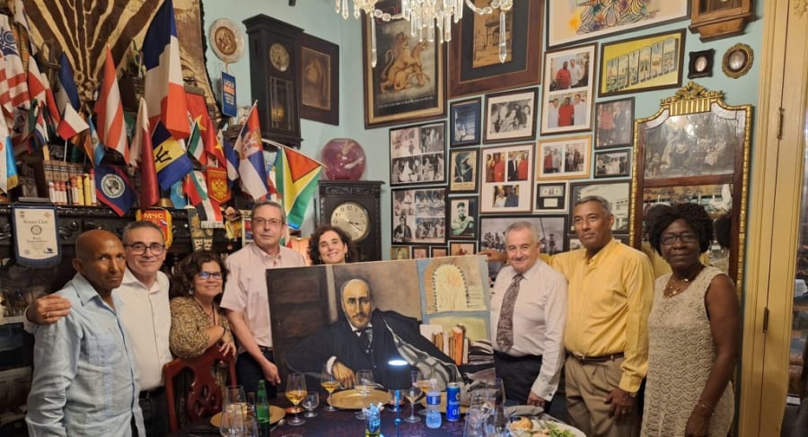Grupo de personas posando frente a una pintura de Santiago Ramón y Cajal, rodeados de banderas, fotos y recuerdos en un ambiente decorativo.