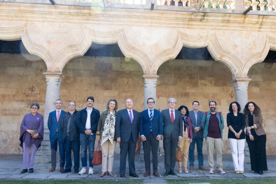 Grupo de personas posando en el patio de una institución, con columnas y arcos arquitectónicos de fondo.