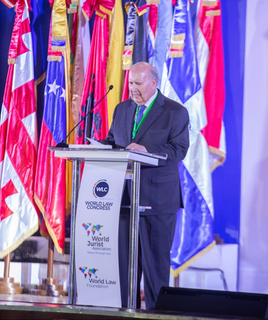 Un orador en un podio durante el Congreso Mundial de Derecho, con banderas de diferentes países al fondo.