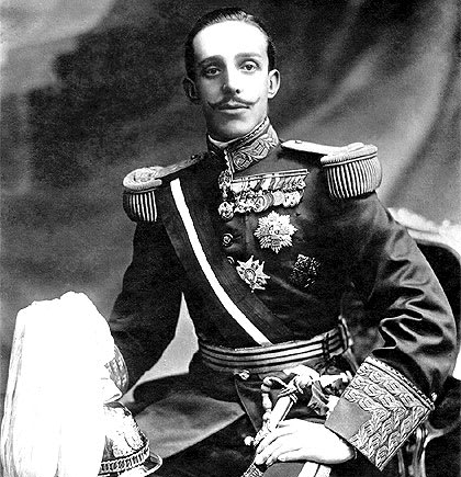 Retrato del rey Alfonso XIII de España en uniforme militar, mostrando medallas y con una espada, sentado con un fondo decorativo.