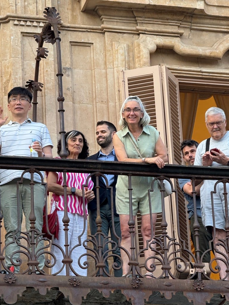 Grupo de participantes y organizadores del curso de Biofísica en la Universidad de Salamanca, sonriendo y posando en un balcón con ventanas de madera de fondo.