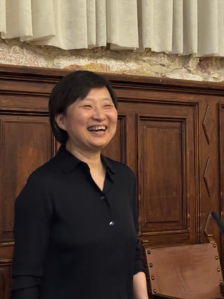 Una científica sonriente durante un evento en la Universidad de Salamanca, con un fondo de madera y cortinas claras.