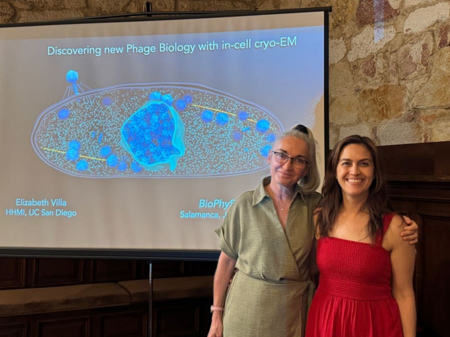 Dos científicas posan frente a una presentación sobre biología de fagos usando criomicroscopía electrónica en un evento académico.