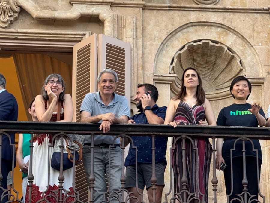Grupo de personas sonriendo y mirando desde un balcón en la Universidad de Salamanca, con arquitectura histórica de fondo.