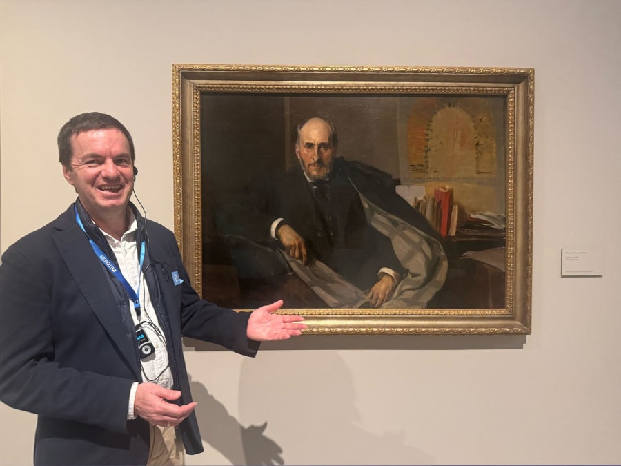 Un visitante sonriente señala un retrato en una galería de arte, mientras el fondo presenta elementos decorativos simples.