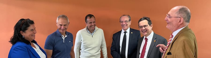 Un grupo de seis personas sonríe y conversan en un ambiente informal, con una pared de fondo de color naranja.