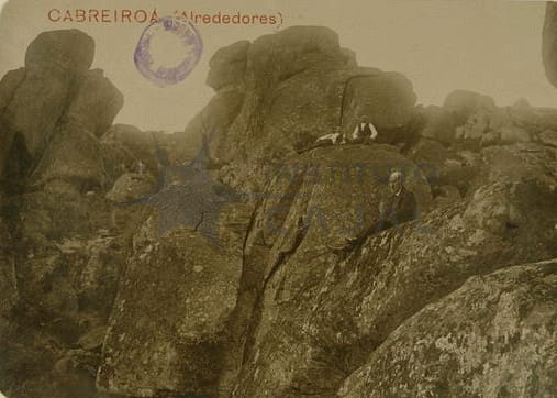 Un paisaje de rocas en los alrededores de Cabreiroá, con un hombre sentado entre las piedras en una fotografía antigua.