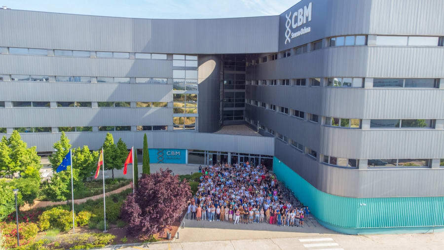 Grupo de personas reunidas frente al edificio del CBM, con banderas de diferentes países y árboles verdes alrededor.