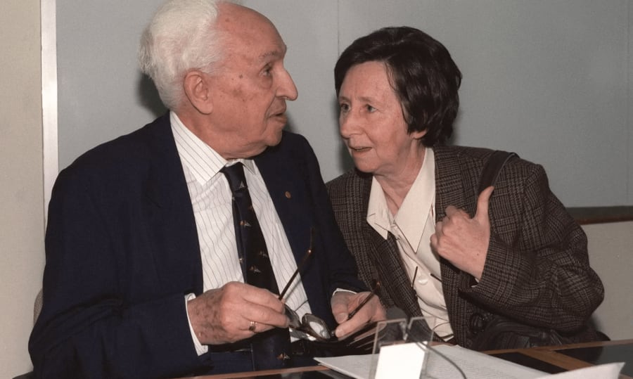 Severo Ochoa conversando con una colega en un evento, ambas personas parecen involucradas en una conversación intensa y amena.