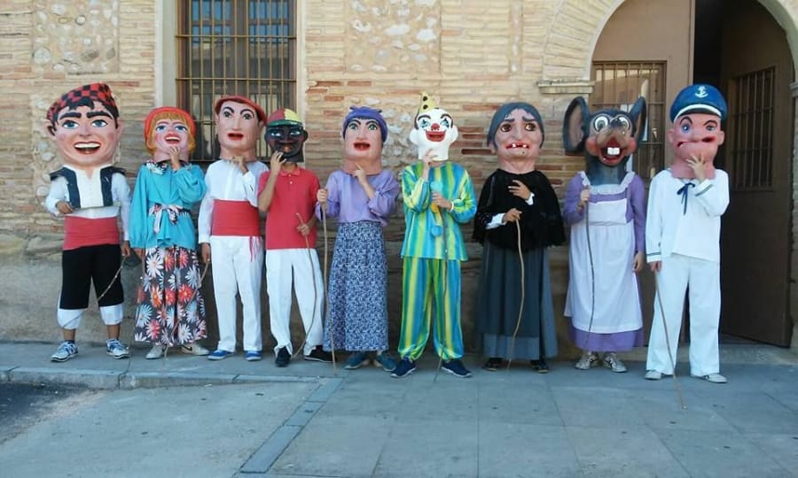 Grupo de gigantes y cabezudos en una calle, representando personajes festivos con disfraces coloridos y máscaras grandes.