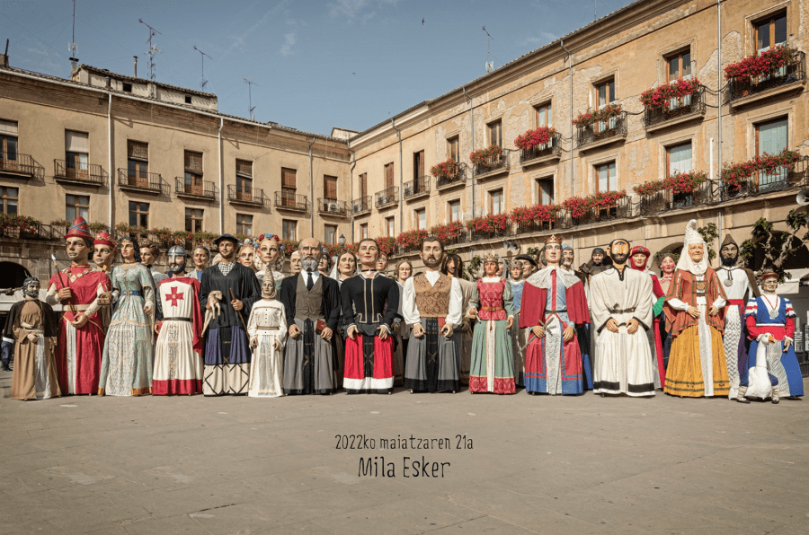 Un grupo de gigantes y cabezudos en una plaza, representando personajes históricos y culturales de España.