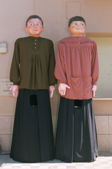 Dos figuras gigantes de madera vestidas con camisas amplias y pantalones negros, representando a personajes típicos de festividades culturales en España.