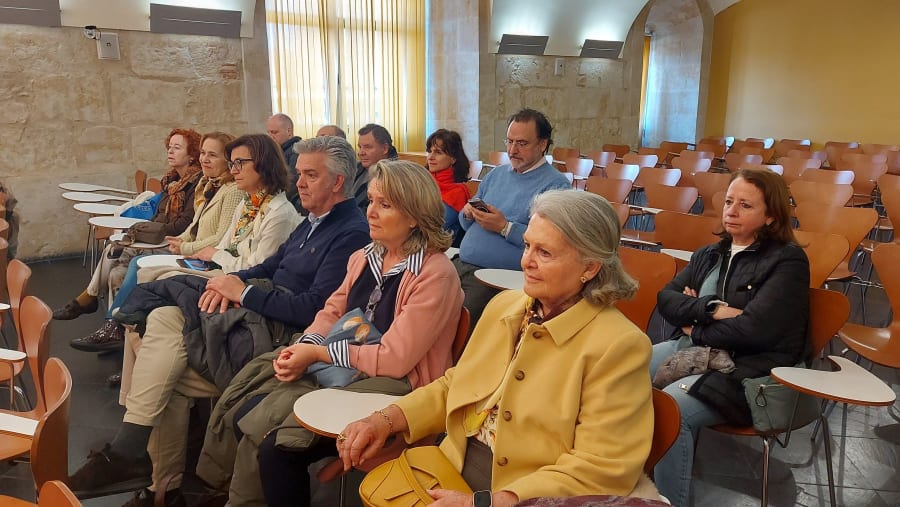 Asistentes sentados en un aula durante una conferencia en la Universidad Pontificia de Salamanca, con mesas y sillas visibles.