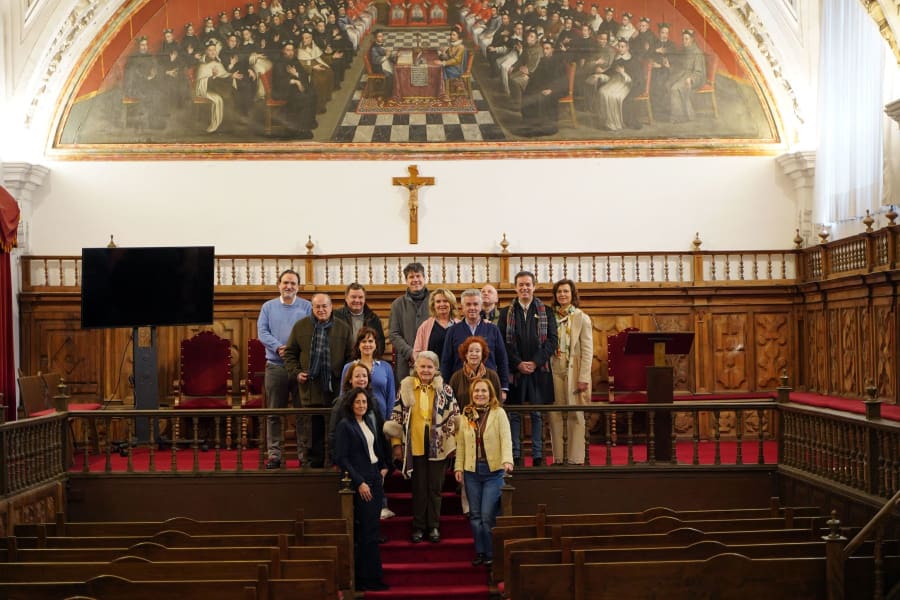 Grupo de personas posando en el Aula Magna de la Universidad Pontificia de Salamanca, con un gran mural histórico en la pared detrás.