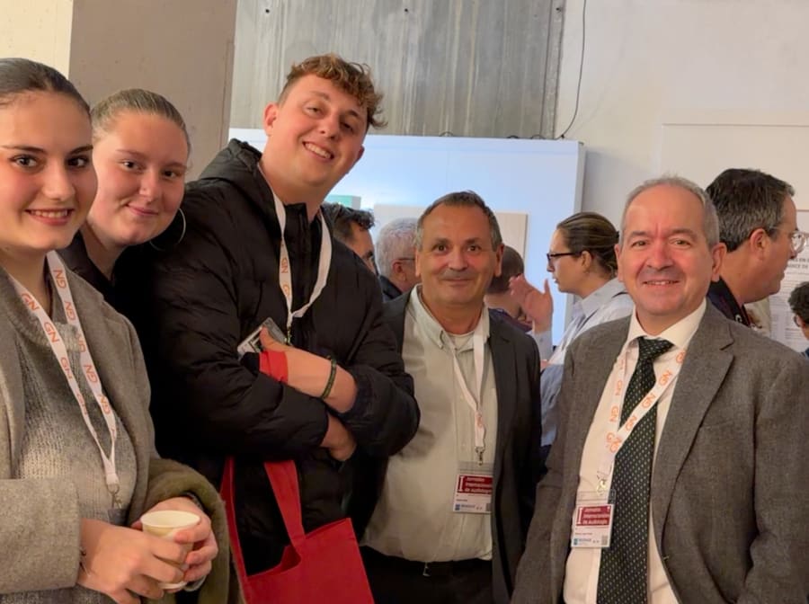 Grupo de participantes sonrientes en un evento de audiología, posando para la cámara, con un ambiente de reunión profesional de fondo.