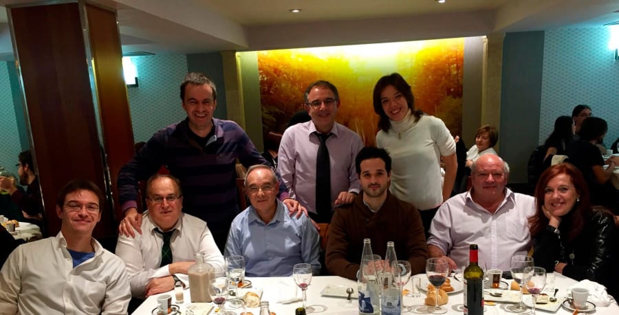 Grupo de personas sonriendo y posando para la foto en un restaurante, con mesas decoradas y copas en la mesa.