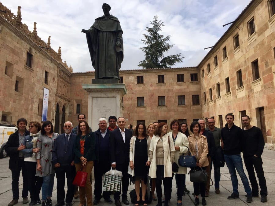 Grupo de personas posando frente a una estatua en un edificio histórico, con un cielo nublado al fondo.