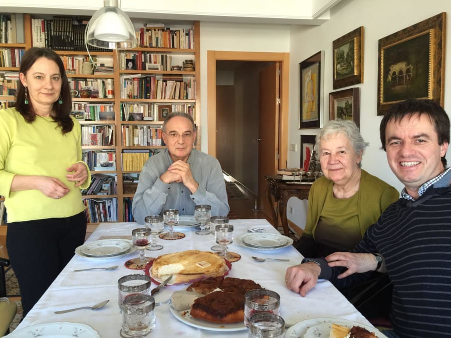Cuatro personas sentadas alrededor de una mesa con comida, en un ambiente acogedor con estanterías llenas de libros en el fondo.