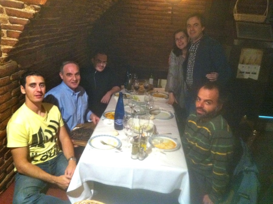 Un grupo de seis personas sentadas alrededor de una mesa en un entorno acogedor con paredes de ladrillo, disfrutando de una comida en un restaurante.