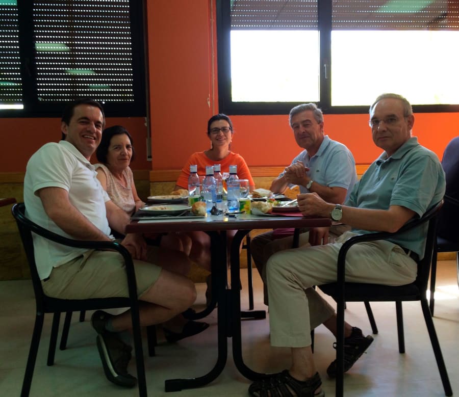 Grupo de personas sentadas alrededor de una mesa en un comedor, compartiendo una comida y sonriendo, con botellas de agua y platos sobre la mesa, en un ambiente acogedor.
