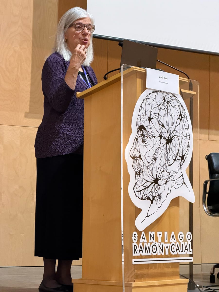 Profesora Linda Hood hablando durante su conferencia en las I Jornadas Internacionales de Audiología en Salamanca, frente a un podio con la imagen de Santiago Ramón y Cajal.