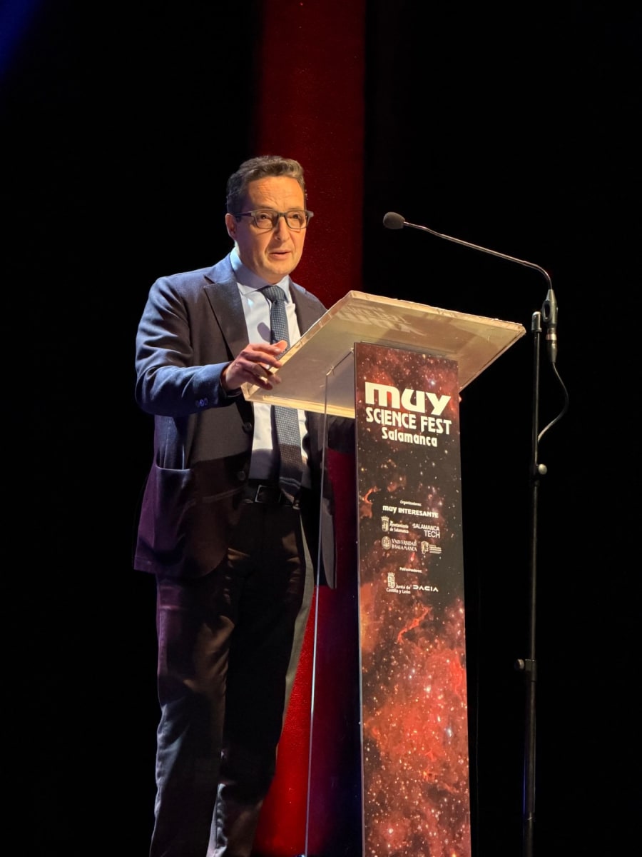 Un presentador de pie detrás de un estrado en el MUY Science Fest en el Teatro Liceo de Salamanca, hablando al público con una atmósfera iluminada por luces de escenario.