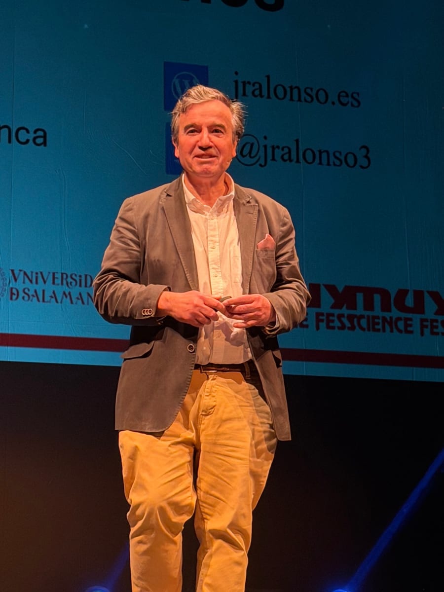 Un ponente de pie en el escenario del MUY Science Fest 2025, sosteniendo un objeto en sus manos, con una pantalla de fondo mostrando información relacionada con la conferencia.