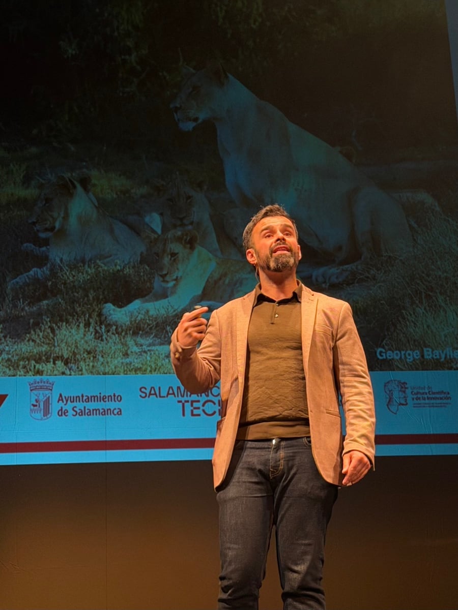 Ponente de pie en el escenario del Teatro Liceo, hablando con pasión mientras se proyecta una imagen de leones en el fondo.