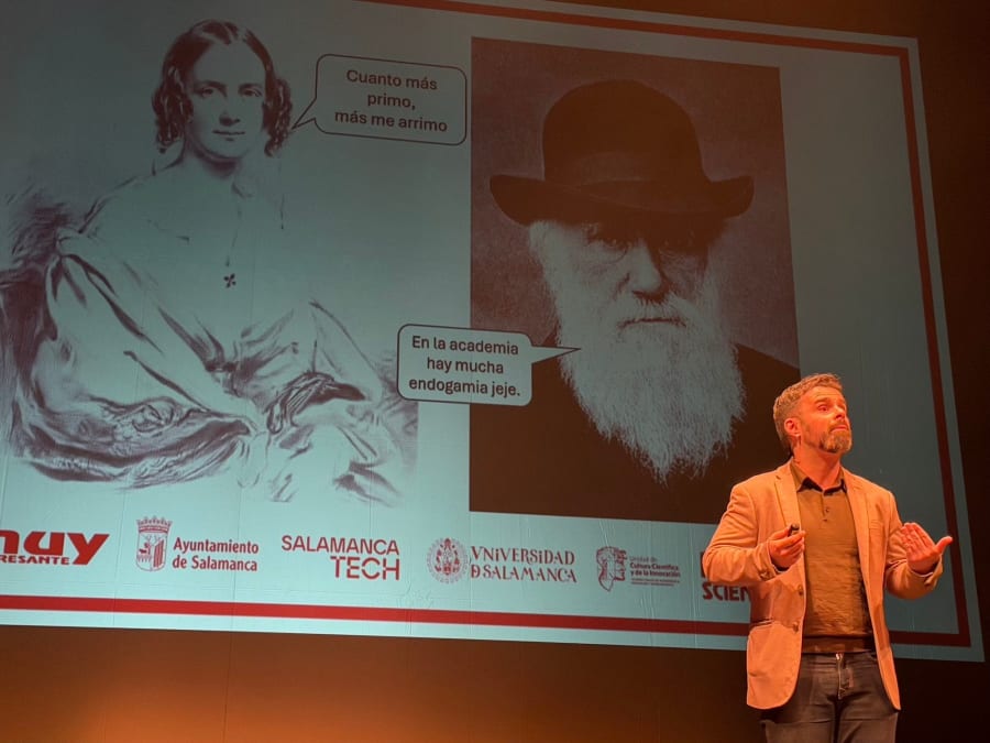 Presentador en el escenario del Teatro Liceo, Salamanca, durante el MUY Science Fest 2025, con imágenes de una mujer y Charles Darwin en el fondo. La mujer dice: