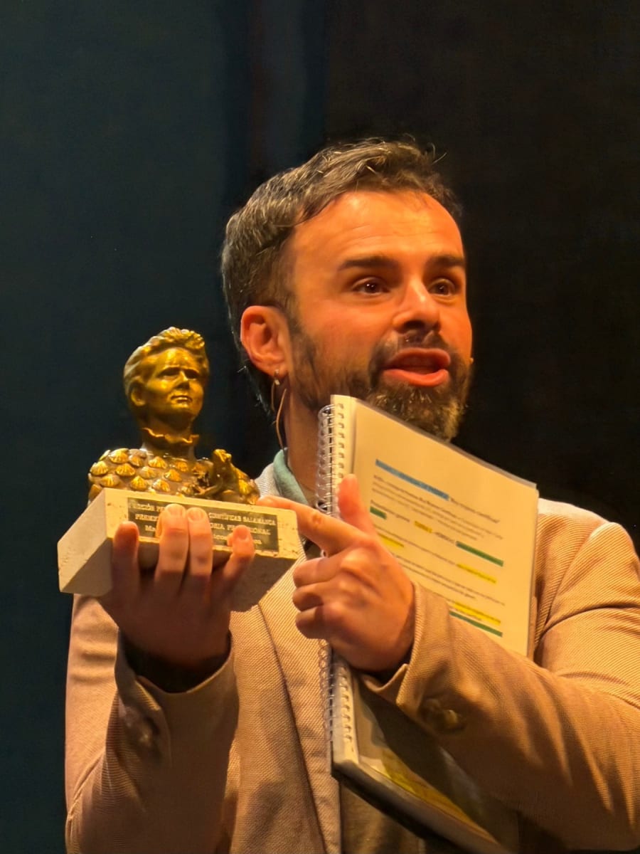 Presentador sosteniendo un trofeo dorado en un evento de ciencia, mostrando entusiasmo y dirección hacia la audiencia.