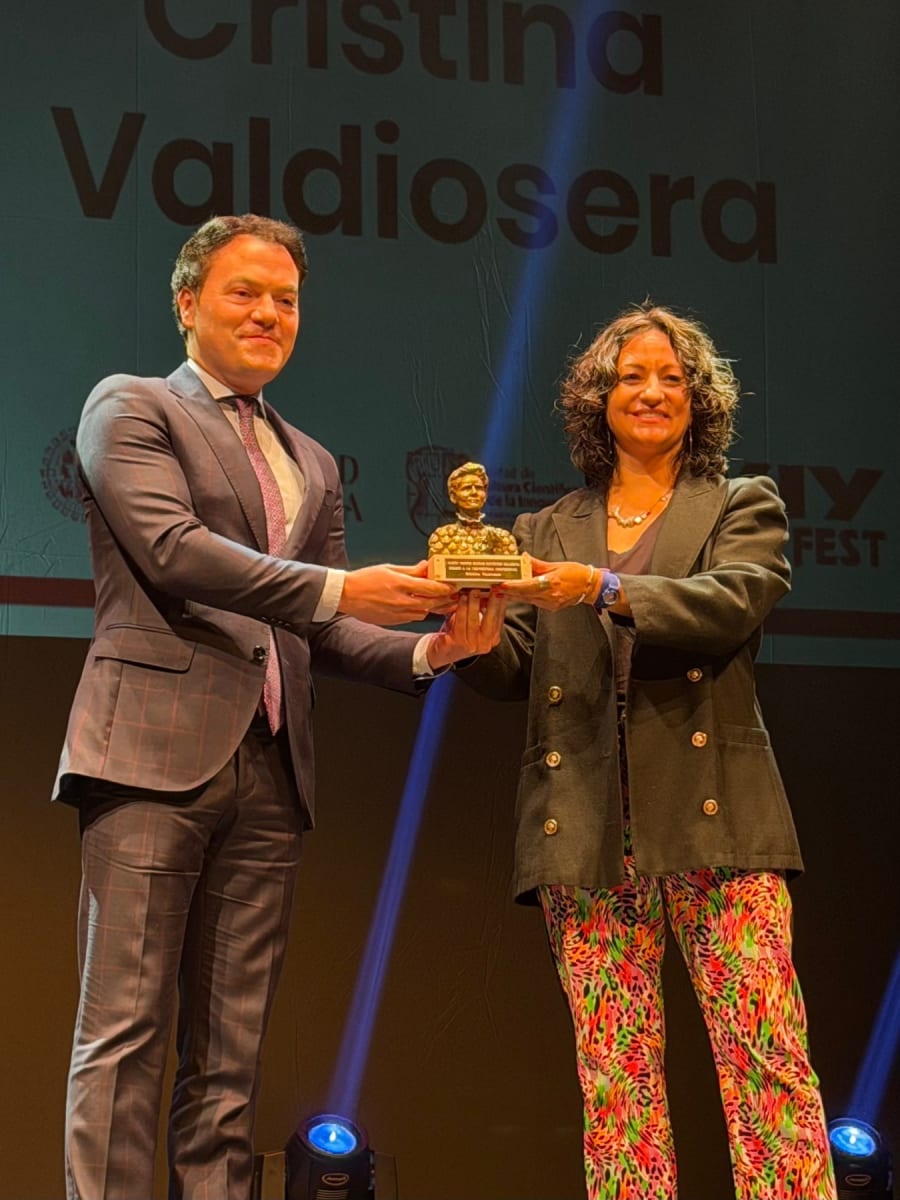 Cristina Valdiosera recibe un premio durante el MUY Science Fest 2025, mientras un hombre se lo entrega. El fondo muestra el nombre de Valdiosera.