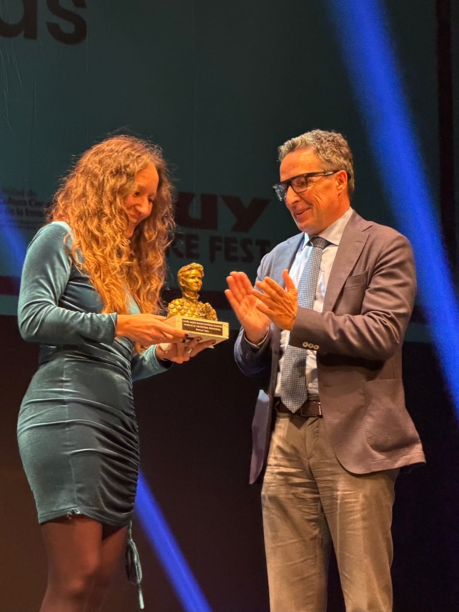 Mujer recibiendo un premio en el escenario durante el MUY Science Fest 2025, con un hombre a su lado aplaudiendo.