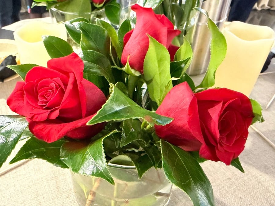 Un ramo de rosas rojas en un jarrón, rodeado de hojas verdes, sobre una superficie clara.