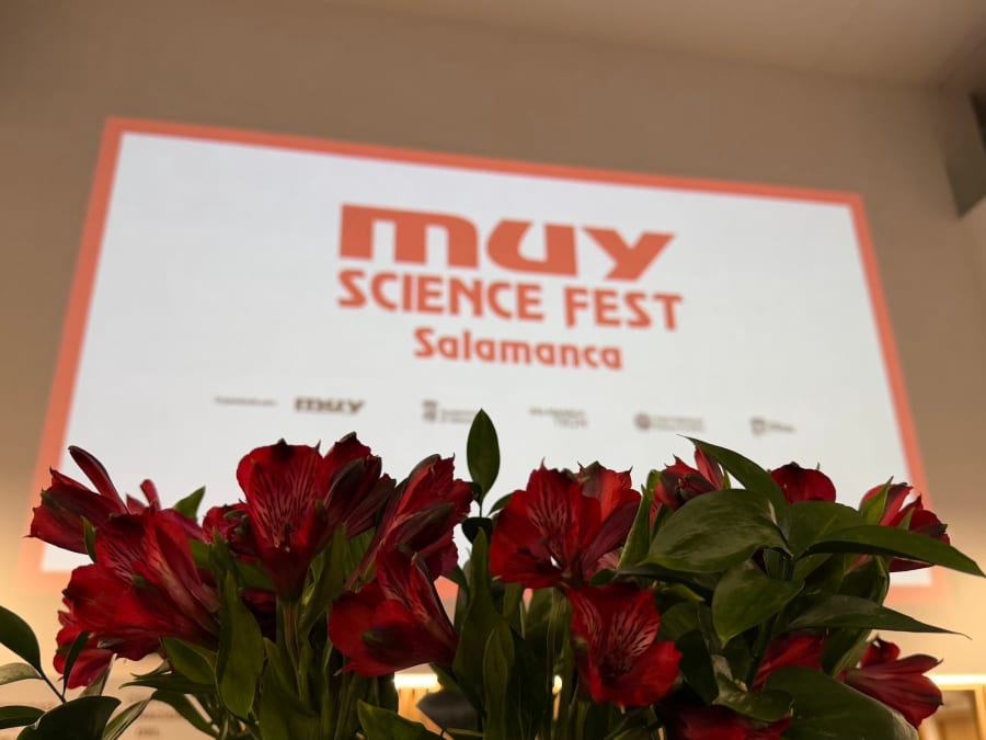 Flores rojas en primer plano frente a un fondo donde se proyecta el logotipo del MUY Science Fest en Salamanca.