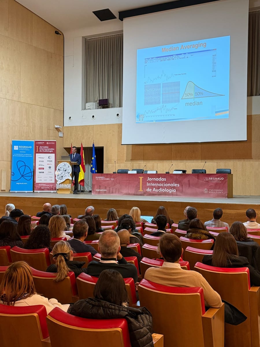 Un conferencista presenta gráficos sobre promediado mediano en el I Jornadas Internacionales de Audiología, mientras la audiencia observa atentamente en un auditorio de Salamanca.