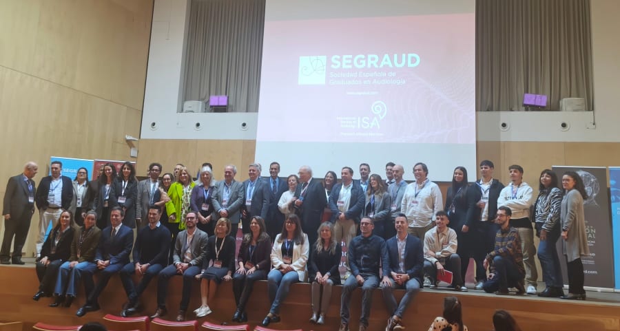 Foto grupal de los participantes en las I Jornadas Internacionales de Audiología en Salamanca, con la presentación de la Sociedad Española de Graduados en Audiología (SEGRAUD) al fondo.