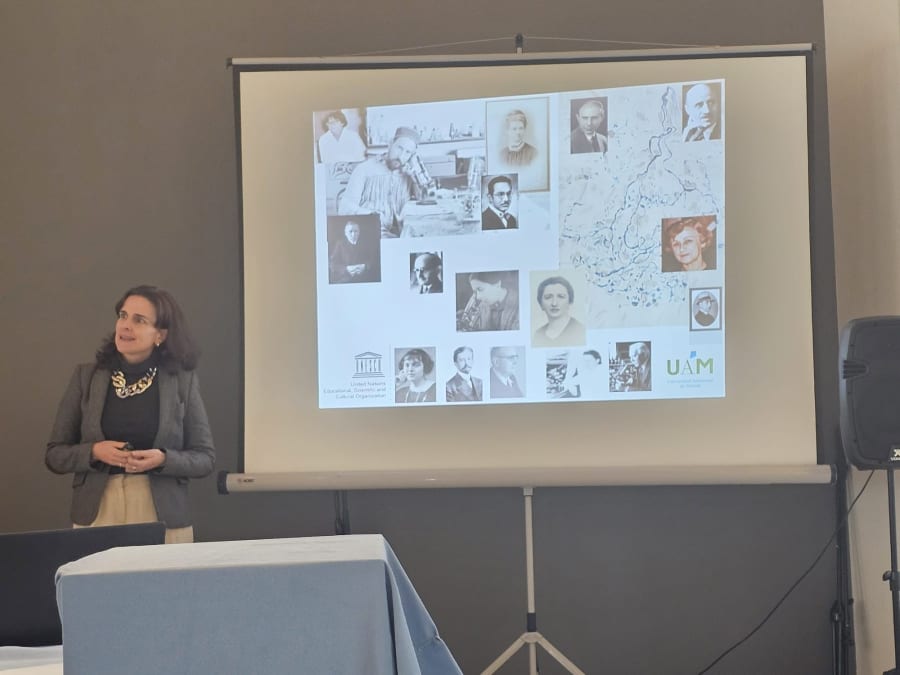 Presentadora en un evento sobre Santiago Ramón y Cajal, junto a una proyección de imágenes históricas de científicos y científicas relacionadas con la neurociencia.
