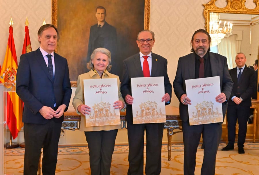 Cuatro personas posando en un salón elegante, sosteniendo documentos con la inscripción 