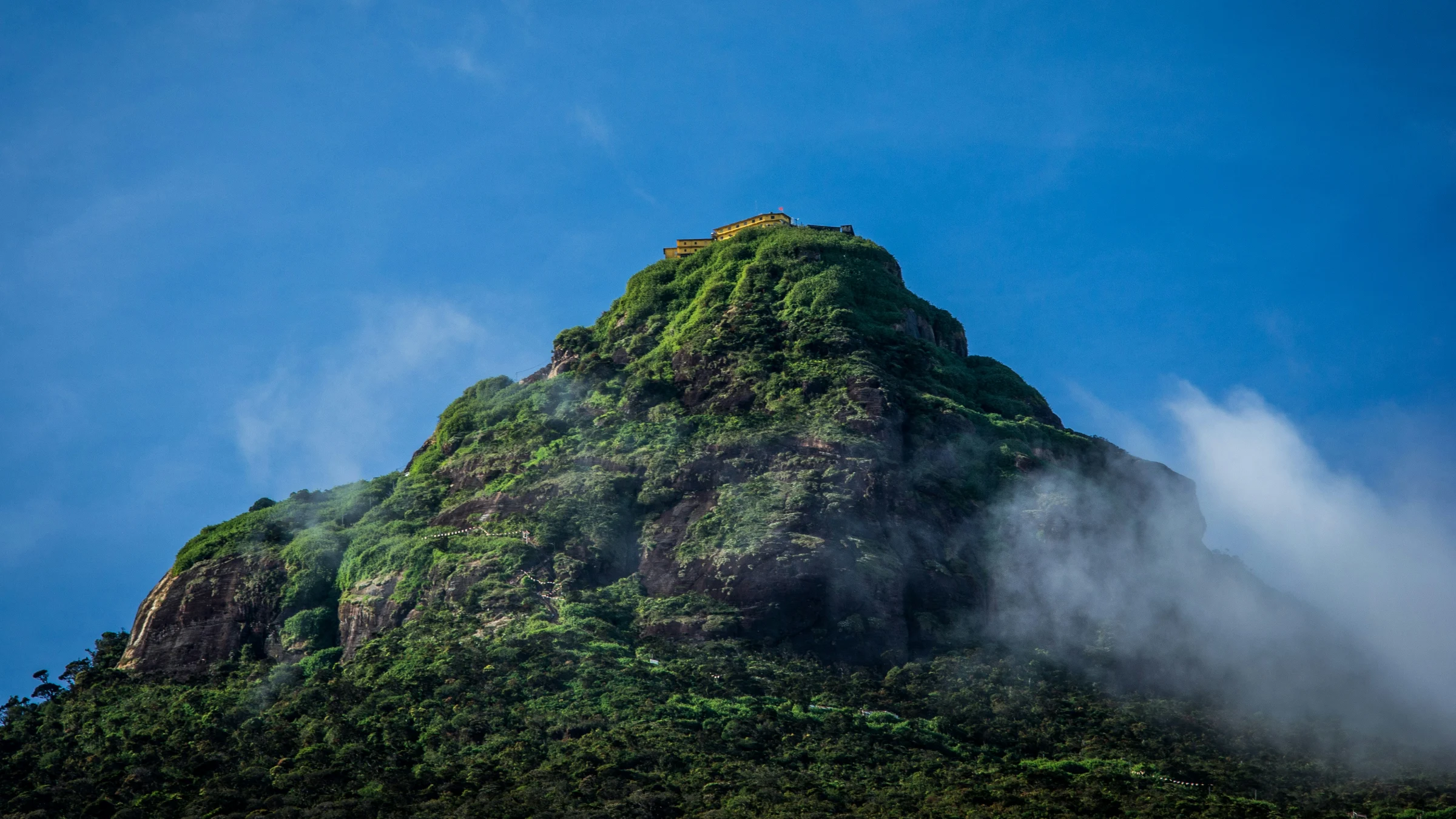 Adam's Peak beklimmen: de kegelvormige top van Sri Pada met de tempel erop, half in de wolken