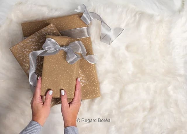 Tapis beige. Cadeaux de Noël. Emballage. Boucles. Mains sur un cadeau. Décembre. Joyeux Noël - Regard Boréal