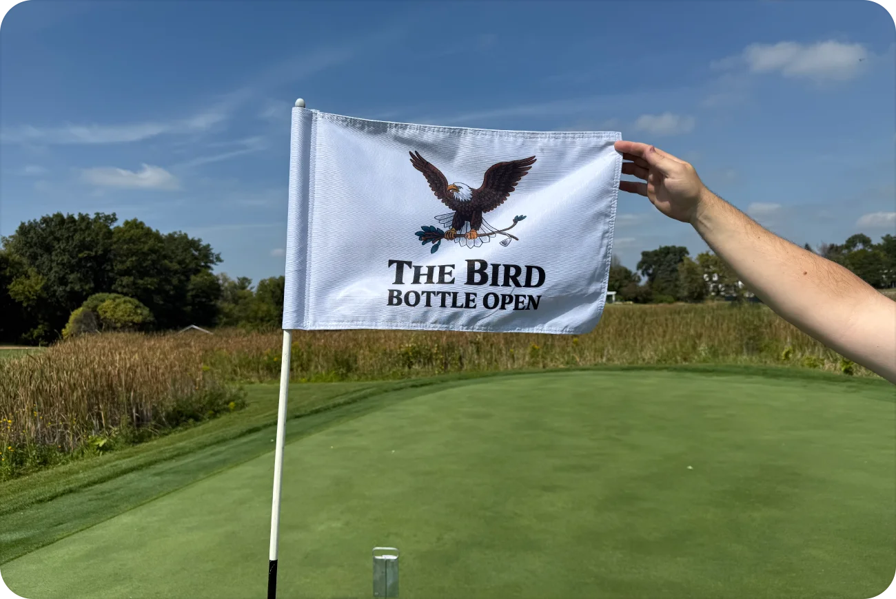Hand holding a Bird Bottle Open flag on a golf course green