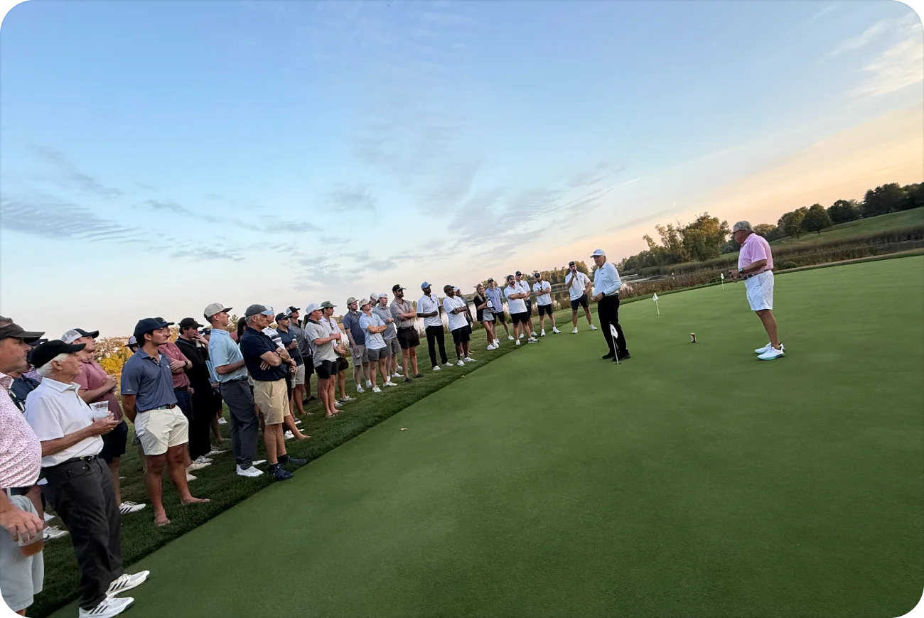 Large crowd of golfers watching Keenan's father speak on the green at sunset