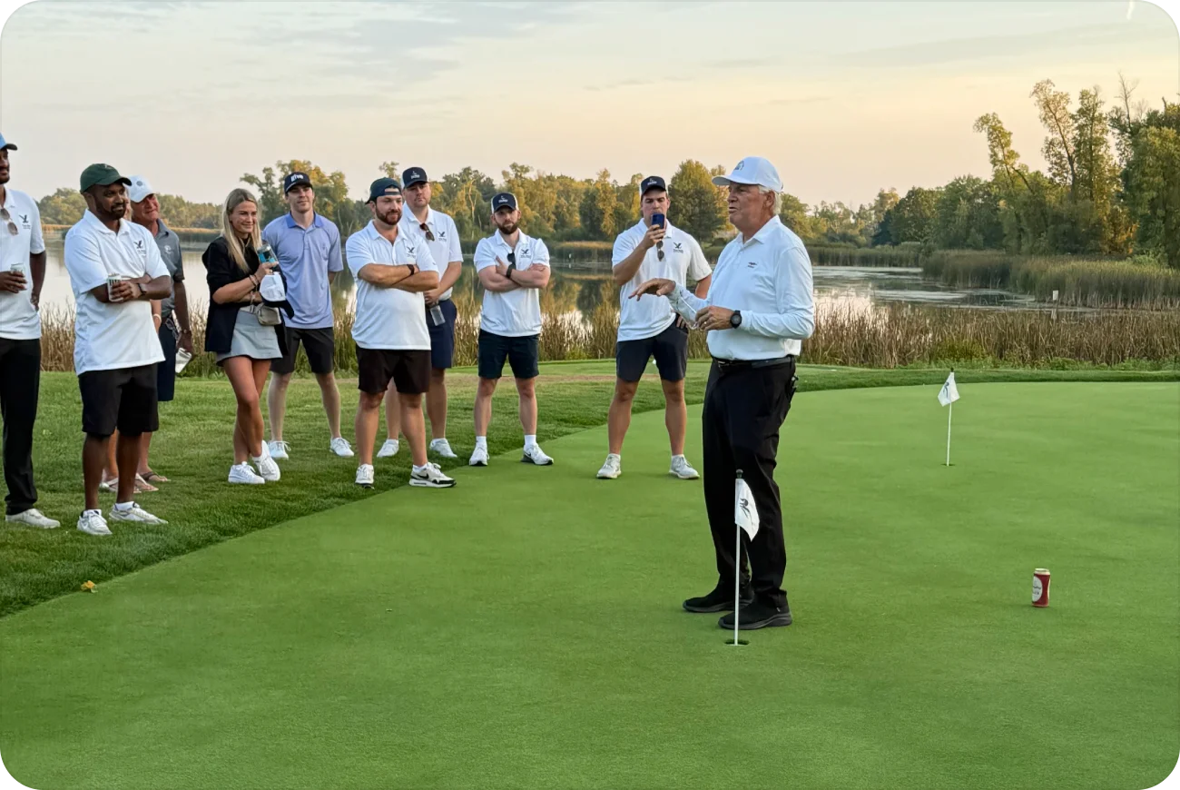 Keenan's father talking to a crowd of golfers on a green with spectators watching at dusk