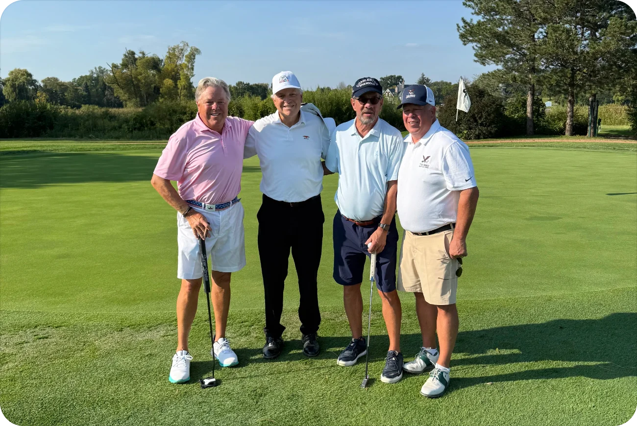 Four men posing together on a sunny golf course green