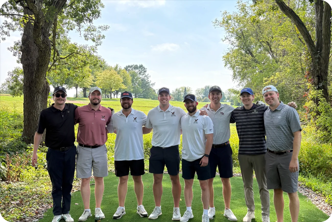 Eight men posing together on a tree-lined golf course fairway