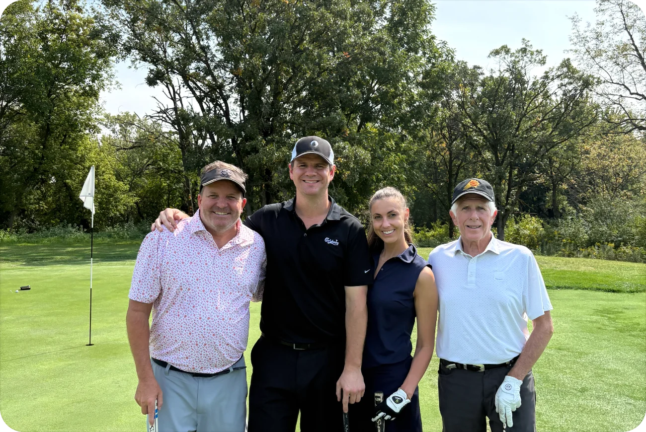 Four golfers — two men, a woman, and a man — posing near a wooded hole