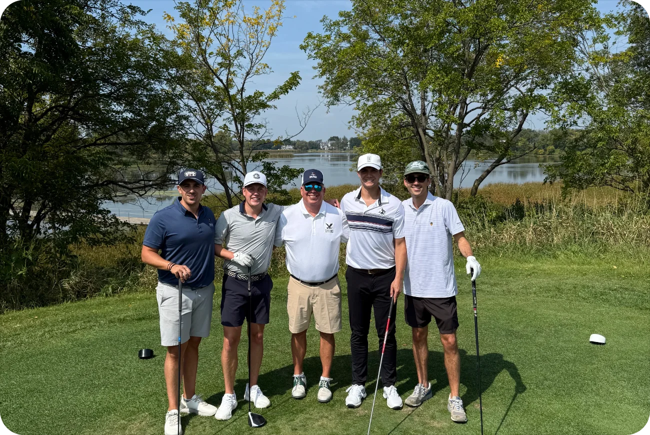 Five men posing together on a golf course with a lake in the background