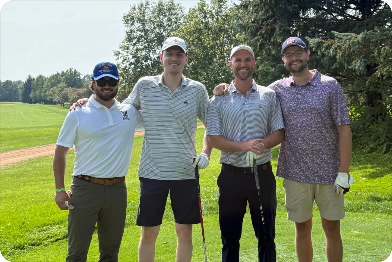 Four men smiling together on a sunny golf course fairway