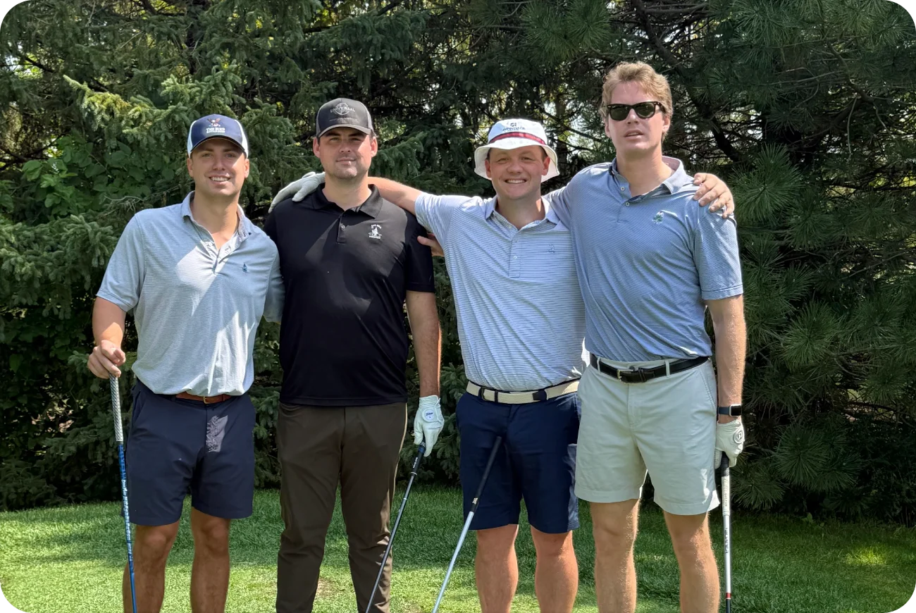 Four men posing together in golf attire near a wooded area